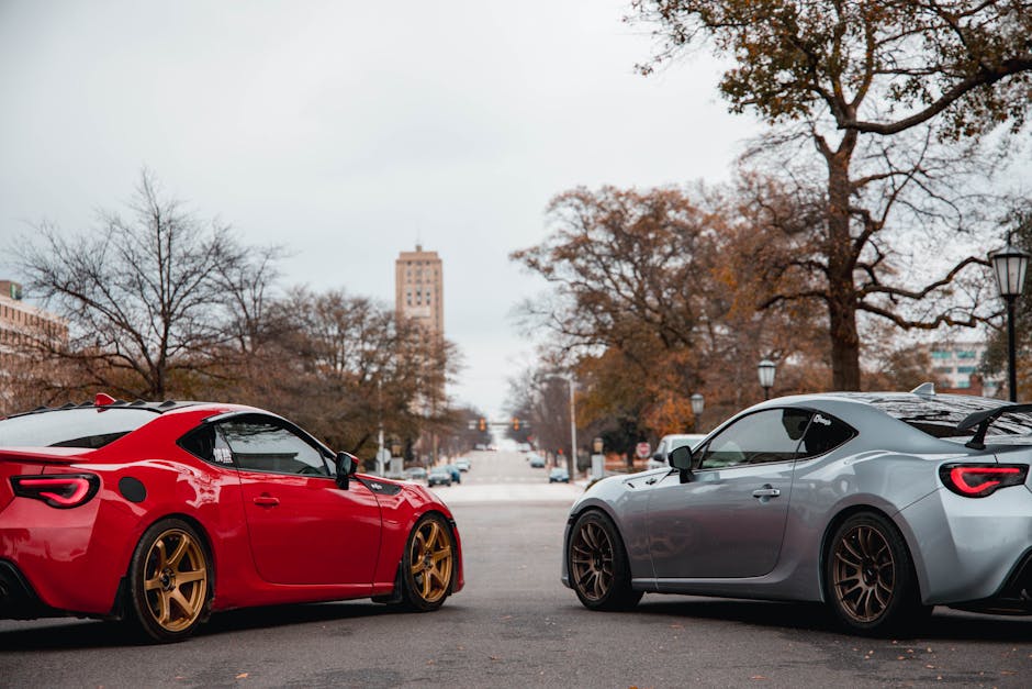 Two luxury sports cars parked on an urban street with trees and buildings in the background.